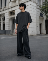 Male model wearing the RENQARA Onyx oversized t-shirt in a full-body street-style look with wide-leg black trousers and sunglasses.