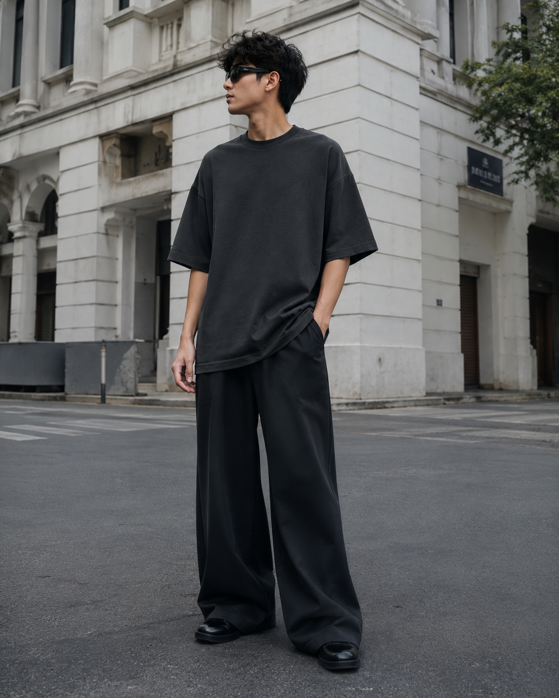 Male model wearing the RENQARA Onyx oversized t-shirt in a full-body street-style look with wide-leg black trousers and sunglasses.