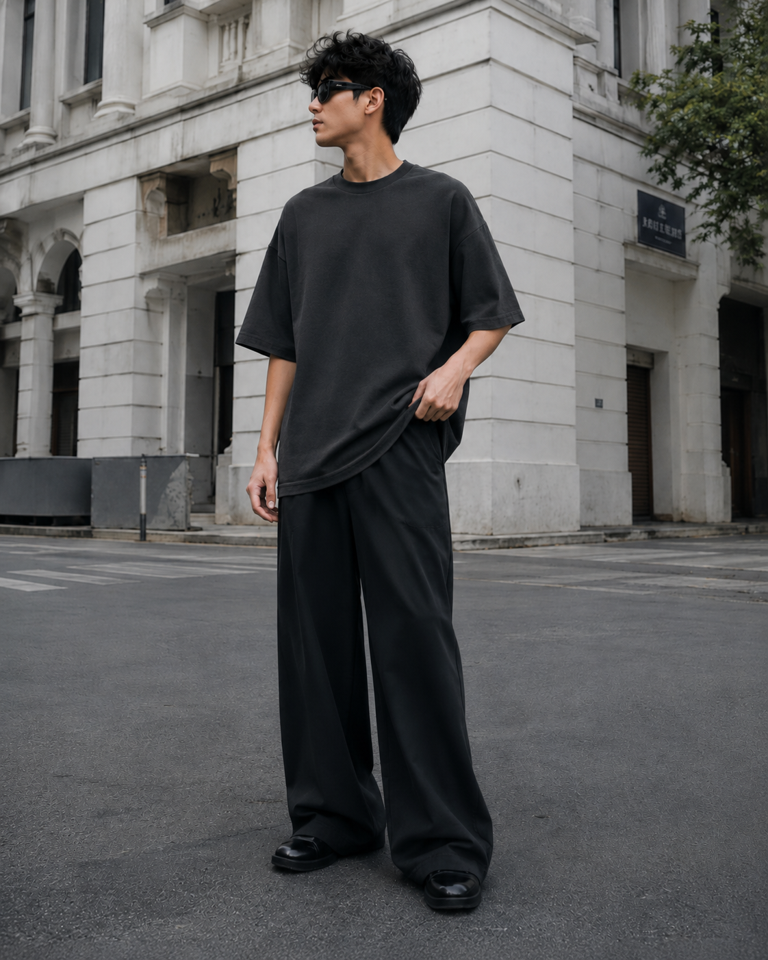 Male model wearing the RENQARA Onyx oversized t-shirt, standing in a relaxed pose and holding the hem to show the oversized fit and drape.