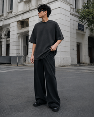 Male model wearing the RENQARA Onyx oversized t-shirt, standing in a relaxed pose and holding the hem to show the oversized fit and drape.
