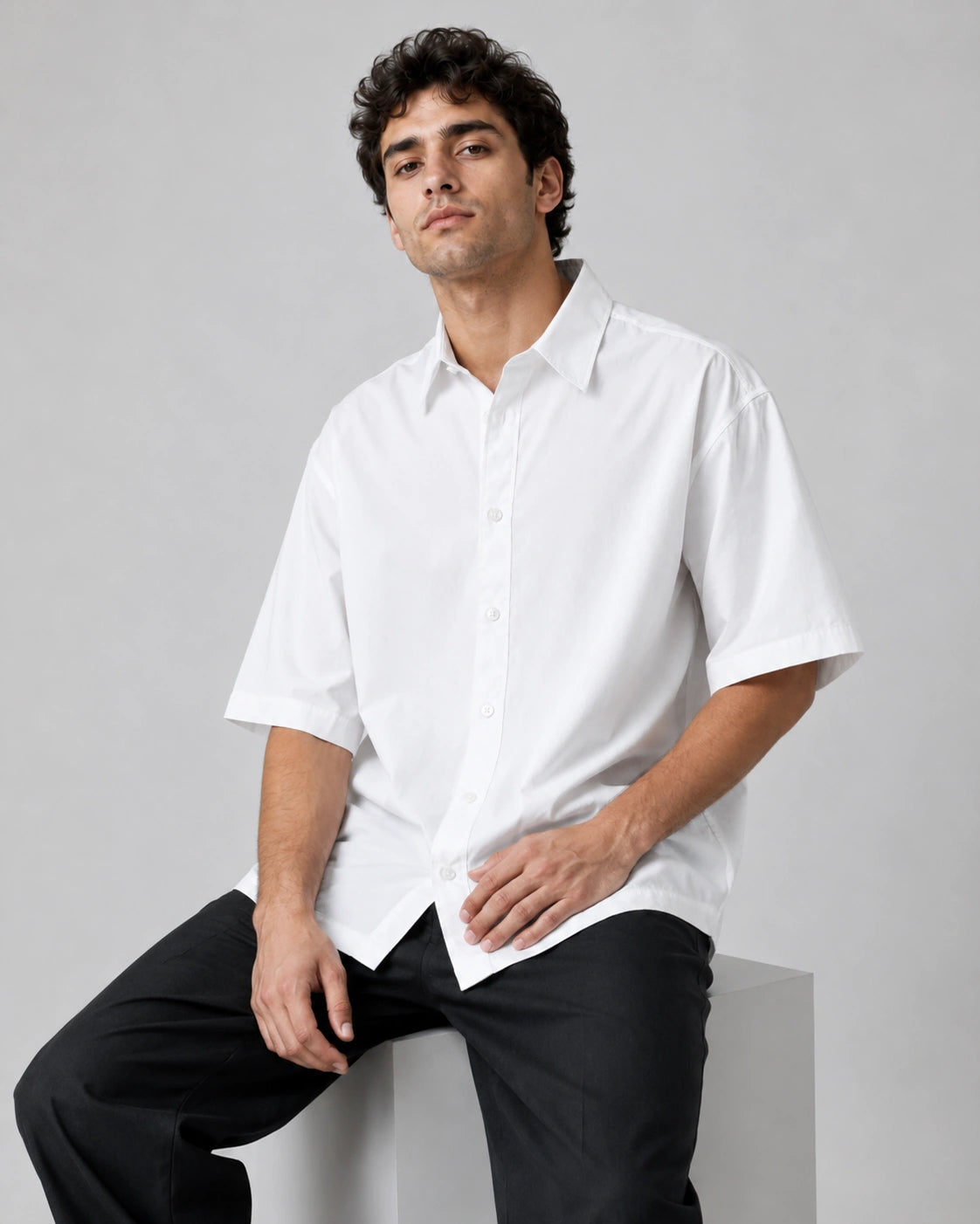 Seated male model in RENQARA White Flow Collar Shirt, a 100% cotton oversized shirt with crisp collar, button front and relaxed fit
